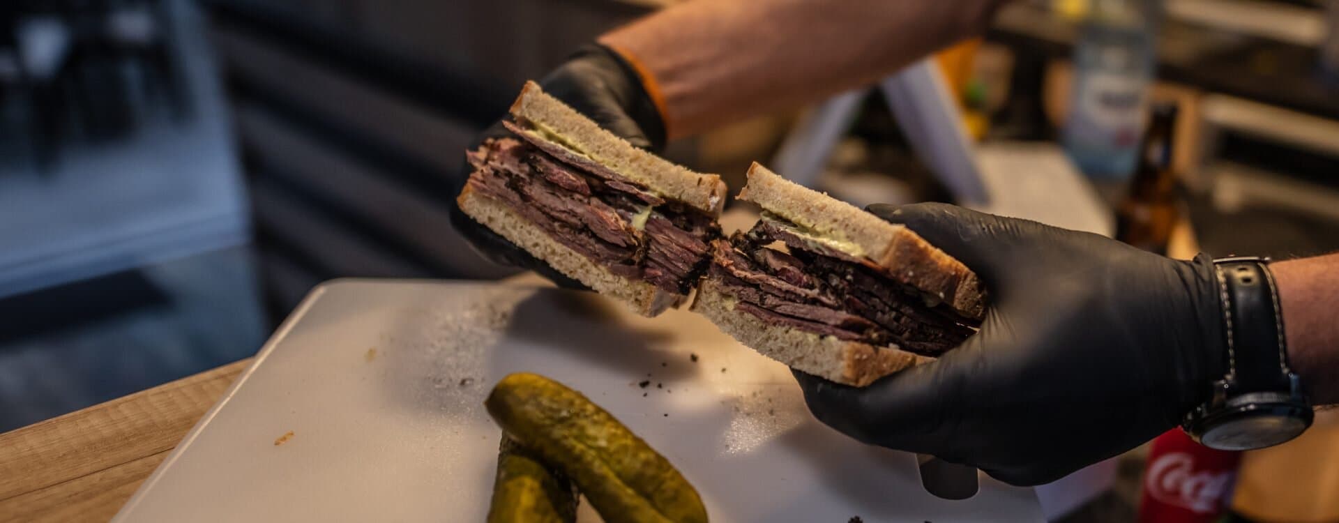 Sandwich cu pastramă de vită ținut în mână, tăiat pe jumătate