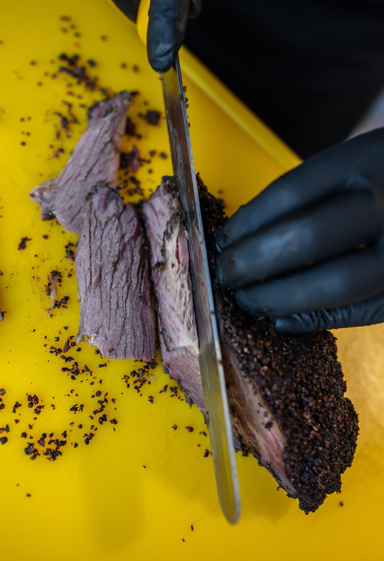 Bucată de pastramă cu crustă de condimente, tăiată felii pe un tocător